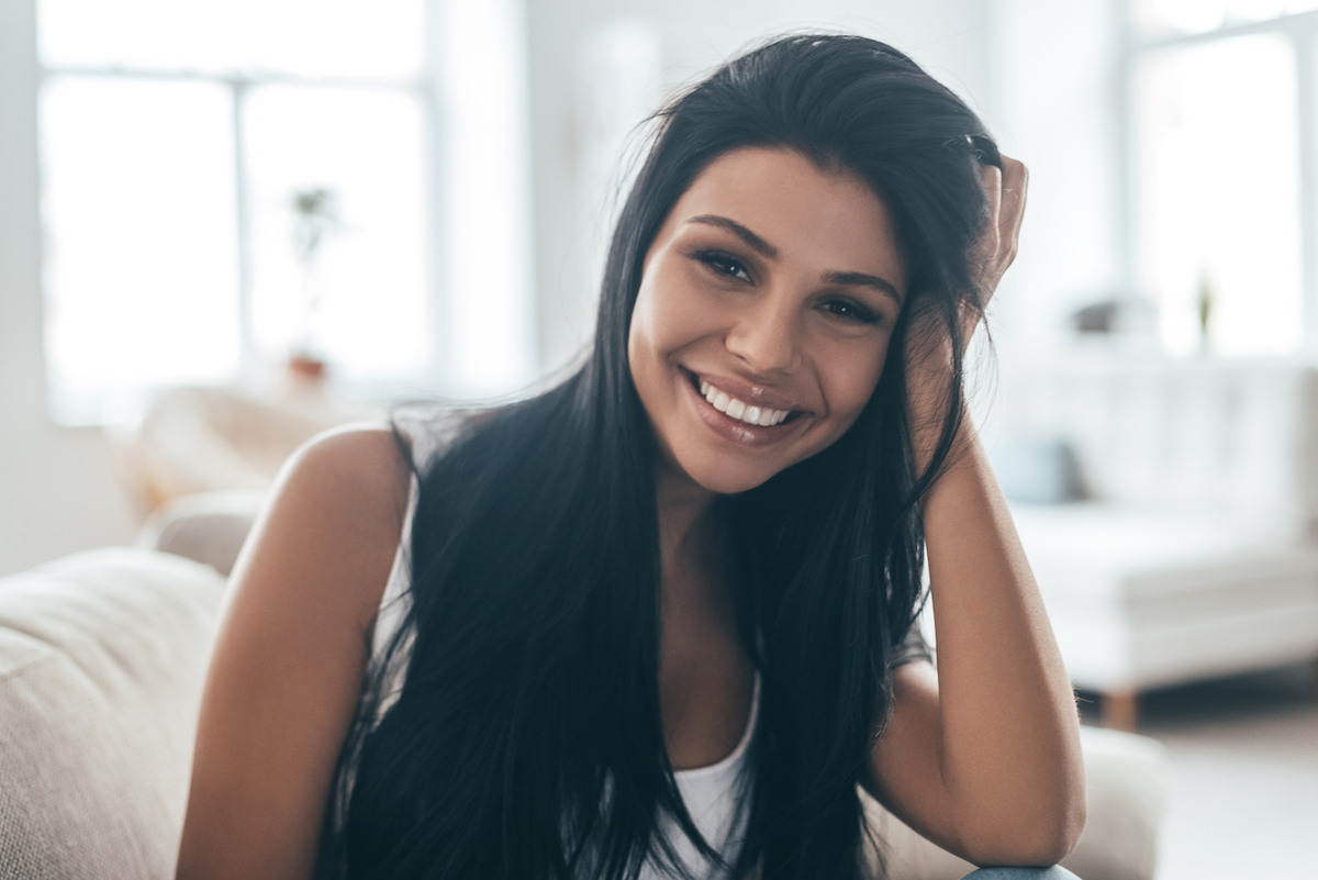 Perfect smile. Portrait of beautiful young woman looking at camera and smiling while sitting on the couch at home